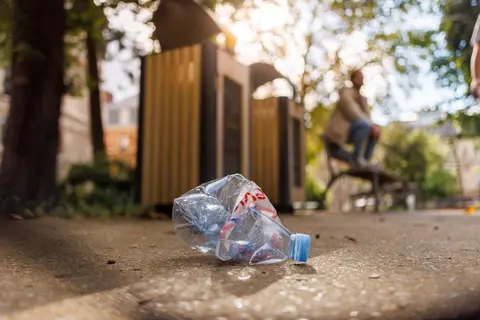 Déchet plastique écrasé au sol devant des conteneurs de tri sélectif