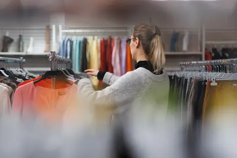Une femme parcourt les portants d'une friperie, examinant des vêtements de seconde main